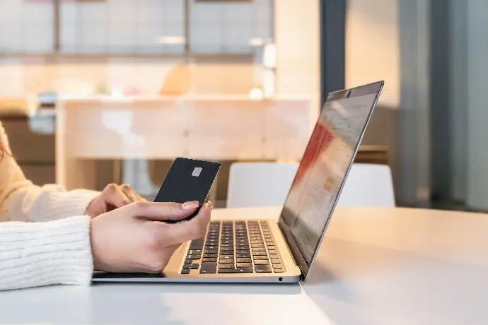 a woman sitting in front of a laptop computer holding a cell phone