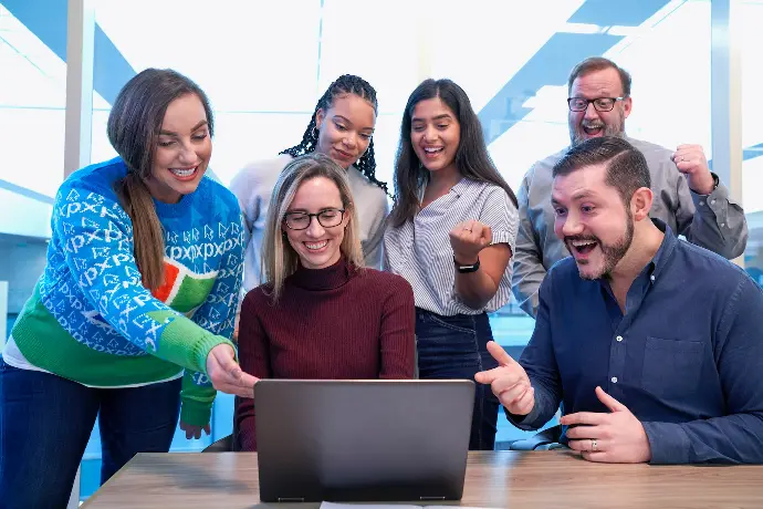 men and women sitting and standing while staring at laptop